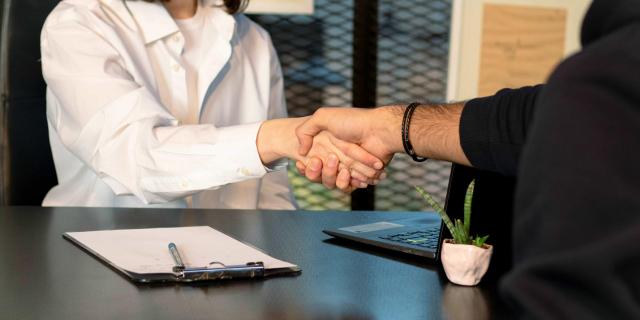 Two people shaking hands sitting on each side of a desk