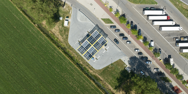 A view from the sky of an EV charging station in a parking lot. The station is covered by a roof composed of solar panels