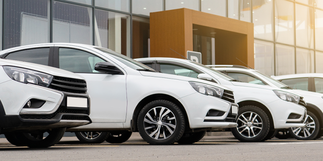 Six white cars are parked in front of a dealership