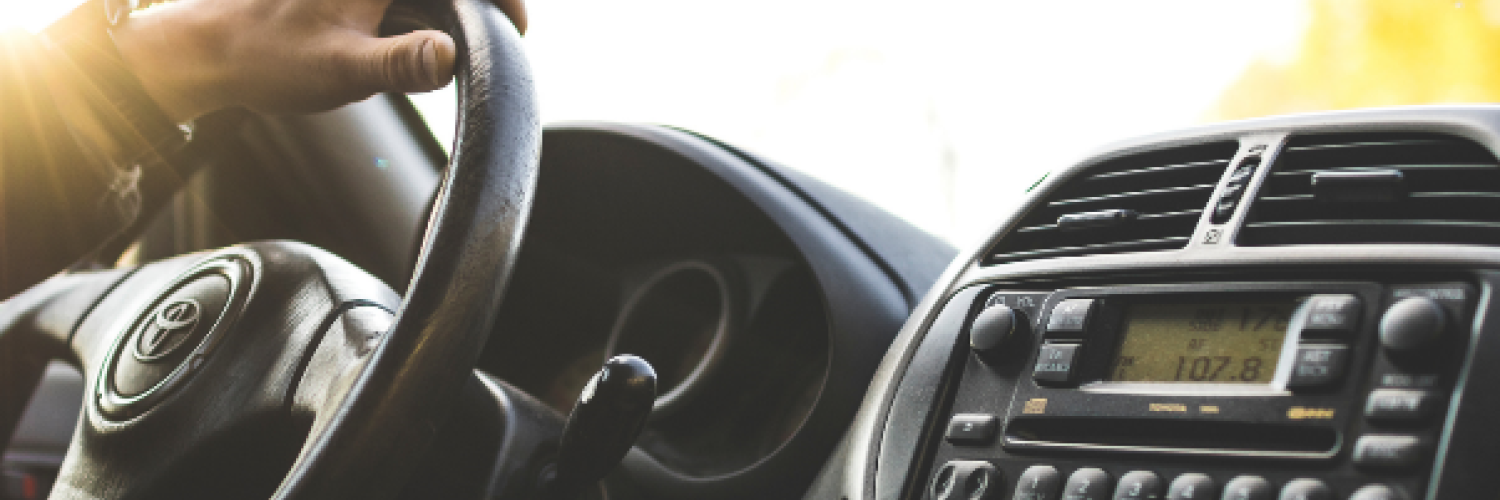 a close up of the steering wheel and the console of a car. A person is driving, we only see his hand on the steering wheel