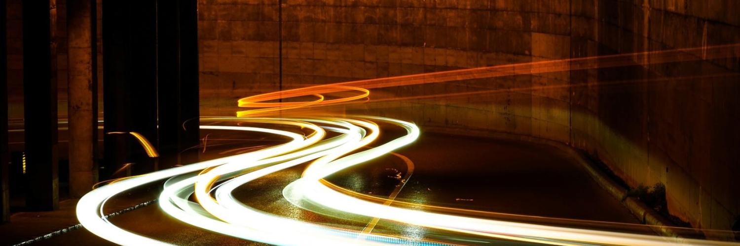 The picture is located inside a tunnel, rays of light are passing through the tunnel representing a car driving inside the tunnel. The light is mainly white but is blue on the right side and red at the back