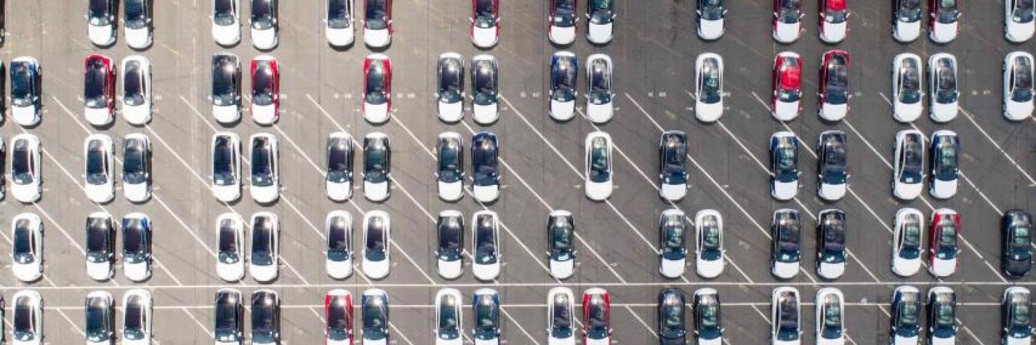 Aerial view of a car storage park where many cars are the same model. Most are white with sunroofs