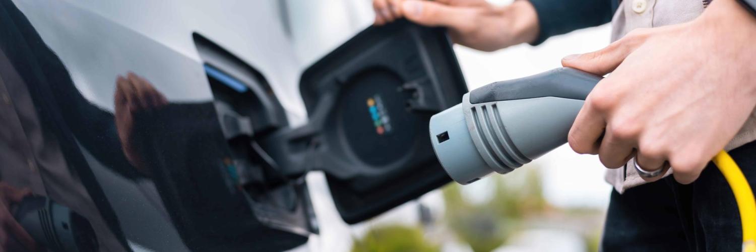 A person is going to charge its electrified vehicle and is currently holding the charger. The view is up close on the hand of the person and the charging port