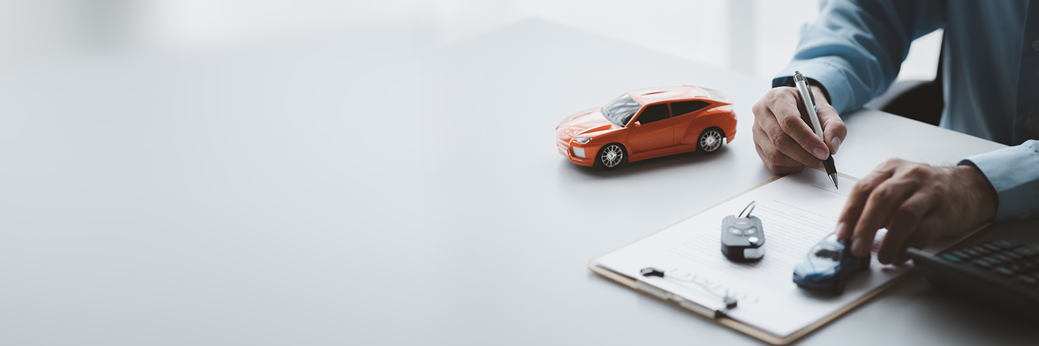 A person at the corner of a desk is signing vehicles papers. We see only his arms and hands, he is holding a pen. Two miniature cars are on the desk.