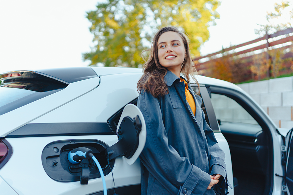 Person next to an EV that is charging A person waiting next to an EV that is charging. She is smiling