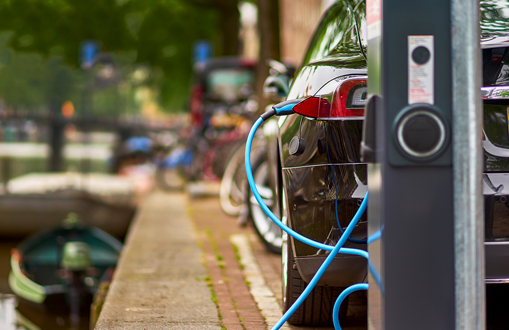 a car charging next to the canal A view of a car from the back with in front of it a charging station. The car is plugged in. It is parked next to the canal in Amsterdam
