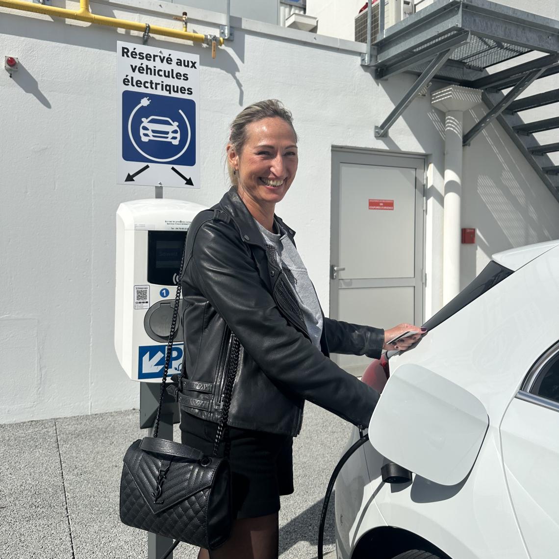 A picture of Christiane who is plugging her PHEV car to charge it. She is on the side, smiling.